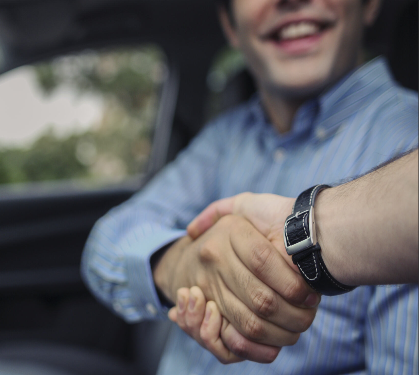 A man sitting in the drivers seat of a car shaking a car dealers hand.
