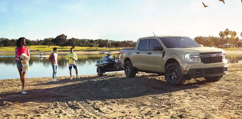 A Family enjoying the day at the beach with a 2025 Ford Maverick nearby backing a Jet ski trailer in to the water.